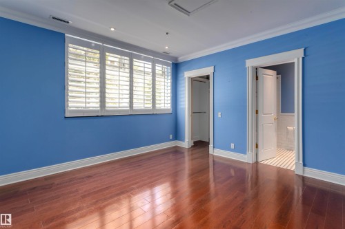 This room features hardwood floors, a large window with white shutters, crown molding, and two doorways - 102 11826 100, Edmonton, AB - Indoor Photo Showing Other Room