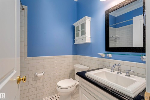 Bathroom featuring a white subway tile wainscoting, a vanity with a dark countertop and white basin sink, and a framed mirror - 102 11826 100, Edmonton, AB - Indoor Photo Showing Bathroom