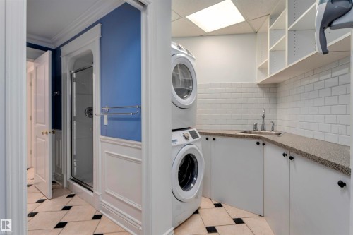 Laundry area featuring stacked washer and dryer, a utility sink, white subway tile backsplash, and built-in shelving - 102 11826 100, Edmonton, AB - Indoor Photo Showing Laundry Room