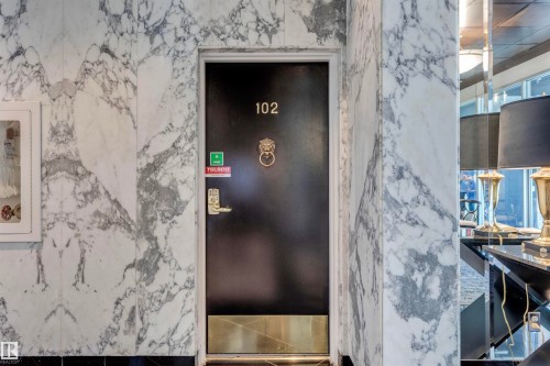 Entrance featuring a dark door with a decorative knocker, complemented by polished marble walls with distinctive veining - 102 11826 100, Edmonton, AB - Indoor