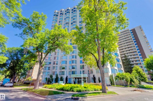 The property features a tall building with numerous windows, complemented by mature trees and landscaped green areas in the foreground - 102 11826 100, Edmonton, AB - Outdoor With Facade