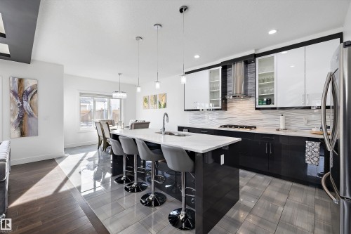 The kitchen features a large island with a white countertop and seating, black cabinetry, and stainless steel appliances - 6303 169 Avenue, Edmonton, AB - Indoor Photo Showing Kitchen With Upgraded Kitchen