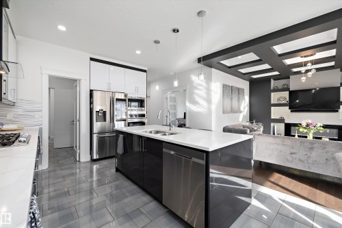 Modern kitchen featuring a spacious island with a white countertop and double sink, stainless steel appliances, and sleek grey tiled flooring - 6303 169 Avenue, Edmonton, AB - Indoor Photo Showing Kitchen With Stainless Steel Kitchen With Double Sink With Upgraded Kitchen