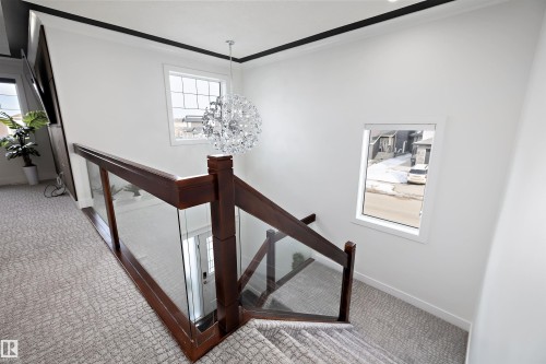 Staircase featuring a modern glass and wood railing, patterned carpet, and a decorative chandelier - 6303 169 Avenue, Edmonton, AB - Indoor Photo Showing Other Room