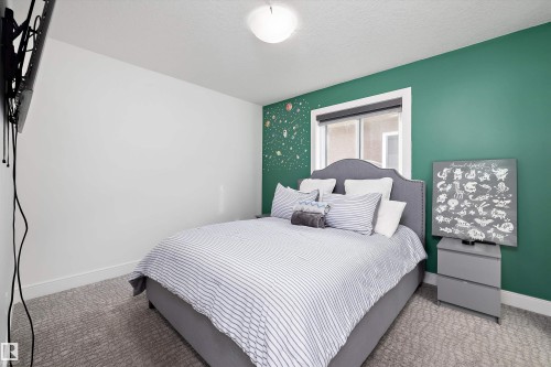 A bedroom with a bed featuring a gray upholstered headboard and striped bedding, set against a green accent wall with decorative elements - 6303 169 Avenue, Edmonton, AB - Indoor Photo Showing Bedroom