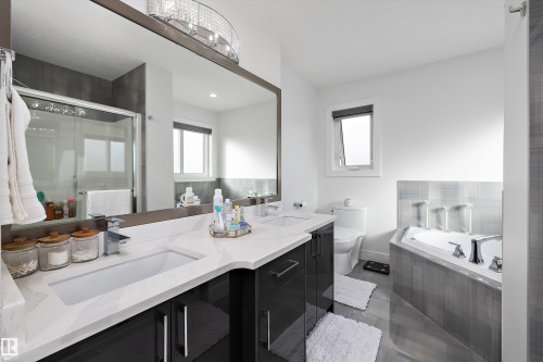 This bathroom features a double vanity with white countertops, a large mirror, and a corner bathtub - 6303 169 Avenue, Edmonton, AB - Indoor Photo Showing Bathroom