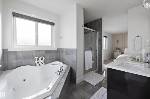 The bathroom features a built-in jetted tub, a window with a roller blind, a glass-enclosed shower, and a vanity with a white countertop and an integrated sink - 6303 169 Avenue, Edmonton, AB - Indoor Photo Showing Bathroom