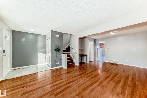 Unfurnished living room with stairs, light wood-type flooring, and a textured ceiling - 11609 125 Street, Edmonton, AB - Indoor