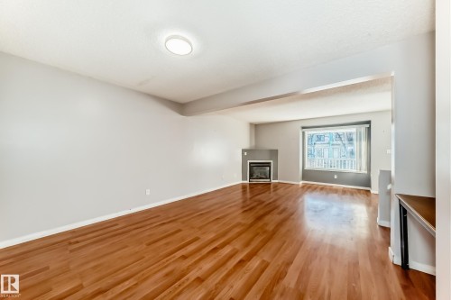 Unfurnished living room featuring a glass covered fireplace, light wood-type flooring, and beam ceiling - 11609 125 Street, Edmonton, AB - Indoor With Fireplace
