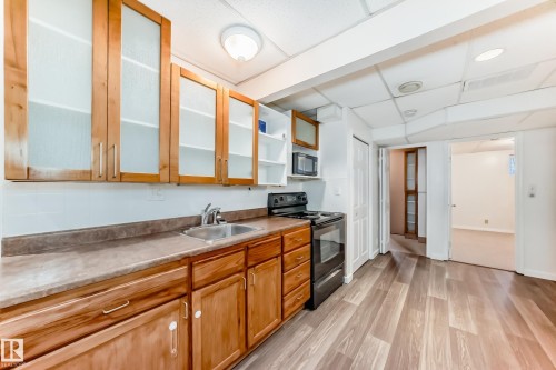 Kitchen with black appliances, a drop ceiling, light wood-style flooring, brown cabinetry, and light countertops - 11609 125 Street, Edmonton, AB - Indoor