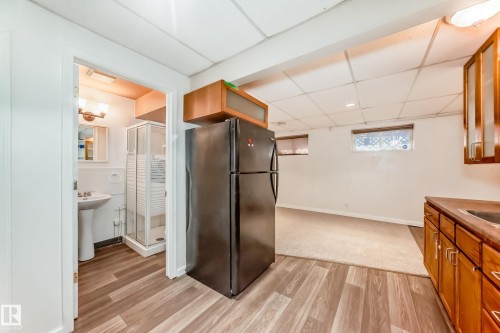 Kitchen with brown cabinetry, freestanding refrigerator, a drop ceiling, light wood finished floors, and glass insert cabinets - 11609 125 Street, Edmonton, AB - Indoor
