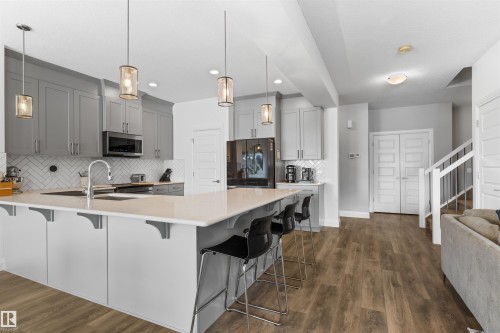 The kitchen features a large island with a light-colored countertop, gray upper and lower cabinetry, a stainless steel microwave, and pendant lighting - 4917 Charles Point(E), Edmonton, AB - Indoor Photo Showing Kitchen With Double Sink With Upgraded Kitchen