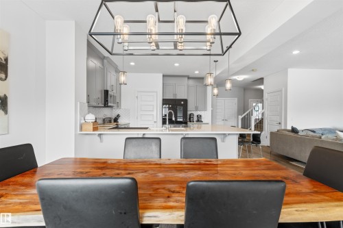 Kitchen and dining area featuring a large central island with seating, pendant lighting, and light grey cabinetry - 4917 Charles Point(E), Edmonton, AB - Indoor Photo Showing Dining Room