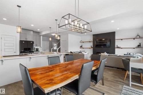 Open-concept living area featuring a kitchen with light grey cabinetry, a dining space with a unique wooden table, and a living room with a dark accent wall and built-in shelving - 4917 Charles Point(E), Edmonton, AB - Indoor Photo Showing Dining Room