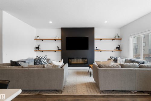 Living area featuring a modern black accent wall with a mounted television and a sleek electric fireplace - 4917 Charles Point(E), Edmonton, AB - Indoor Photo Showing Living Room With Fireplace