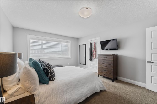 The bedroom features neutral-toned walls and carpet flooring, a large window with blinds, and a white paneled door - 4917 Charles Point(E), Edmonton, AB - Indoor Photo Showing Bedroom