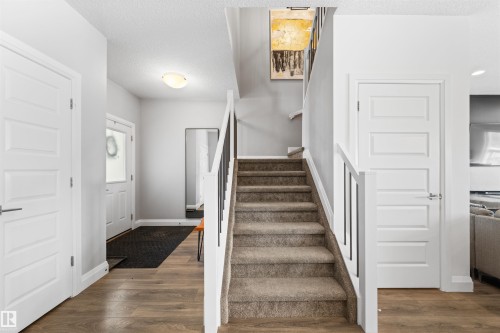 Inviting entryway featuring light wood-look flooring, a carpeted staircase with white and black railings, and white interior doors - 4917 Charles Point(E), Edmonton, AB - Indoor Photo Showing Other Room