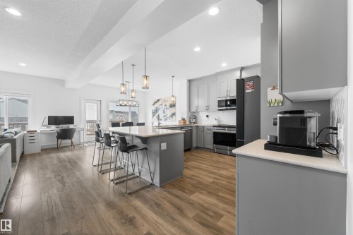 The property features an open-concept living area with wood-look flooring, a kitchen island with seating, pendant lighting, and a kitchen equipped with stainless steel appliances and light grey cabinetry - 4917 Charles Point(E), Edmonton, AB - Indoor Photo Showing Kitchen With Upgraded Kitchen