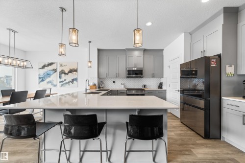 The kitchen features light-toned cabinetry, stainless steel appliances, and a central island with bar seating - 4917 Charles Point(E), Edmonton, AB - Indoor Photo Showing Kitchen With Upgraded Kitchen