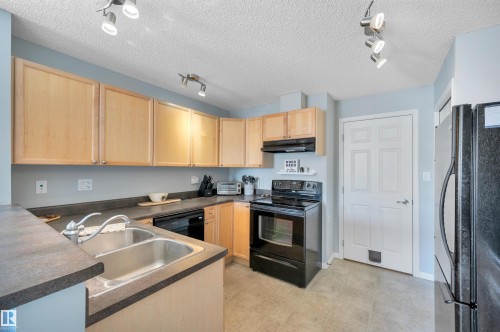 The kitchen features light-toned cabinetry, dark countertops, and a double basin stainless steel sink - 106 3040 Spence Wynd, Edmonton, AB - Indoor Photo Showing Kitchen With Double Sink