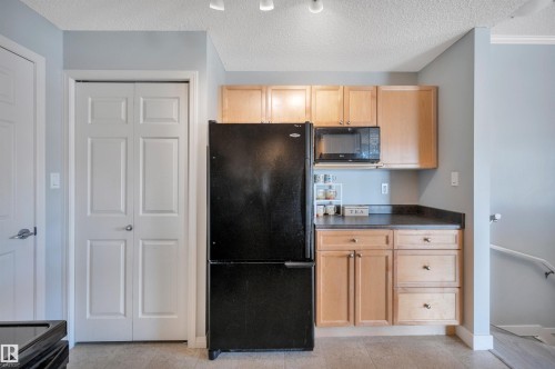 Kitchen area featuring light wood cabinetry, a black refrigerator, a built-in microwave, and a dark countertop - 106 3040 Spence Wynd, Edmonton, AB - Indoor Photo Showing Kitchen