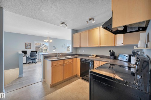 The kitchen features light wood cabinetry, a double basin stainless steel sink, black appliances, and track lighting - 106 3040 Spence Wynd, Edmonton, AB - Indoor Photo Showing Kitchen With Double Sink