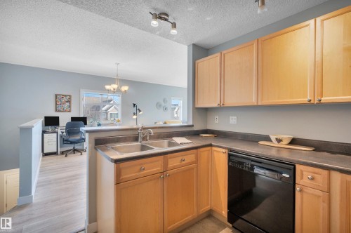 Kitchen featuring wood cabinetry, a stainless steel double sink, and a black dishwasher - 106 3040 Spence Wynd, Edmonton, AB - Indoor Photo Showing Kitchen With Double Sink