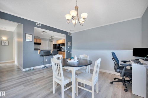 This dining area features light-toned flooring, a modern chandelier, and a convenient pass-through to the kitchen, which includes a breakfast bar with seating - 106 3040 Spence Wynd, Edmonton, AB - Indoor Photo Showing Dining Room