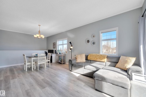 The property features light-colored flooring, windows providing natural light, and a chandelier in the dining area - 106 3040 Spence Wynd, Edmonton, AB - Indoor Photo Showing Living Room