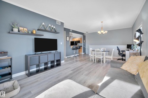 This living space features light-colored flooring, a dining area with a round table and chairs, and a partial view into a kitchen area - 106 3040 Spence Wynd, Edmonton, AB - Indoor Photo Showing Living Room