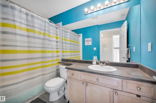 The bathroom features a light wood vanity with a dark countertop and an integrated sink, set against vibrant blue walls - 106 3040 Spence Wynd, Edmonton, AB - Indoor Photo Showing Bathroom