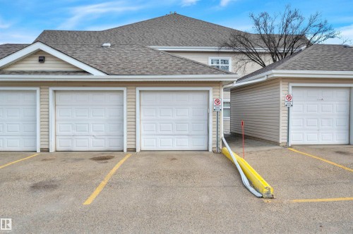 The property offers convenient parking, featuring a paved lot with yellow line markings and multiple white garage doors - 106 3040 Spence Wynd, Edmonton, AB - Outdoor