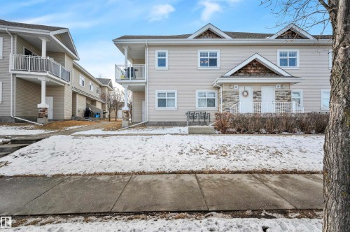 The property features a multi-story exterior with light-colored siding, multiple windows, and a stone facade entrance - 106 3040 Spence Wynd, Edmonton, AB - Outdoor With Balcony With Facade