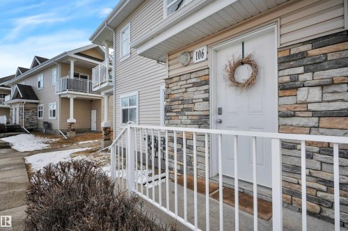 The property features a stone and siding exterior, a front door with a decorative wreath, and a white railing leading to the entrance - 106 3040 Spence Wynd, Edmonton, AB - Outdoor With Balcony With Facade