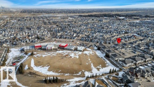 Aerial view of the property and surrounding neighborhood, featuring a large residential area, open fields, and nearby buildings with red roofs - 106 3040 Spence Wynd, Edmonton, AB - Outdoor With View