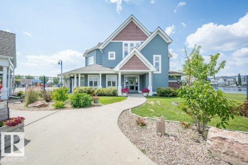The property features a blue exterior with white trim and brown accents, a curved concrete pathway leading to the entrance, and a well-maintained lawn with landscaping - 106 3040 Spence Wynd, Edmonton, AB - Outdoor With Facade