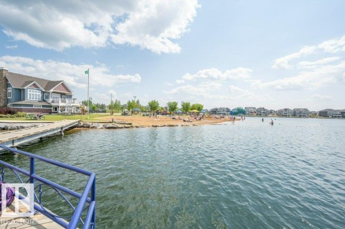 The property features a view of a tranquil lake, a sandy beach, and a dock for water access - 106 3040 Spence Wynd, Edmonton, AB - Outdoor With Body Of Water With View