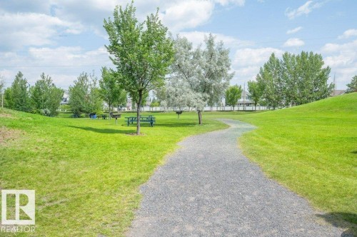 This property is situated in a community with an extensive park area, featuring a gravel pathway, mature trees, and a picnic area with tables - 106 3040 Spence Wynd, Edmonton, AB - Outdoor With View