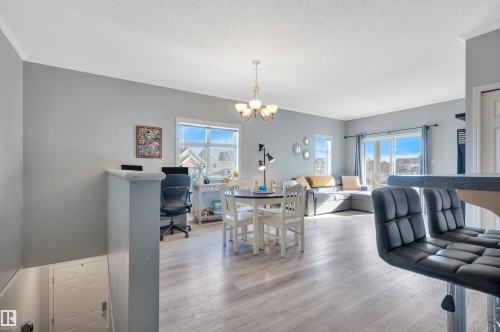 This property features light-colored flooring, a dining area with a chandelier, and a living area with a large window and sliding glass door - 106 3040 Spence Wynd, Edmonton, AB - Indoor