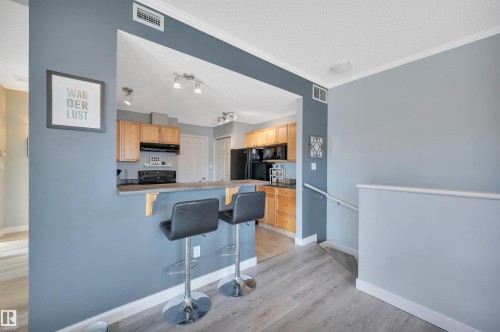 The kitchen features wooden cabinetry and black appliances, complemented by a breakfast bar with seating - 106 3040 Spence Wynd, Edmonton, AB - Indoor Photo Showing Kitchen