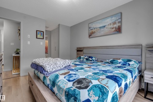 This sleeping area features light-colored flooring, a bed with a light wood frame and an upholstered headboard, and light grey walls - 128 390 Windermere Road, Edmonton, AB - Indoor Photo Showing Bedroom