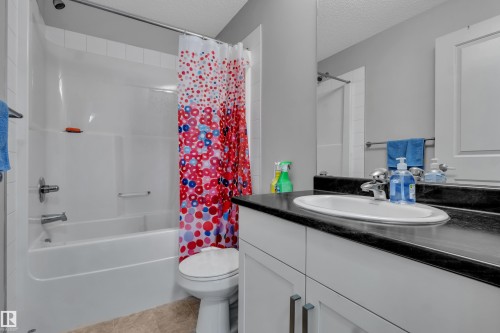 Bathroom featuring a white vanity with a dark countertop, an integrated sink, and a mirror - 128 390 Windermere Road, Edmonton, AB - Indoor Photo Showing Bathroom