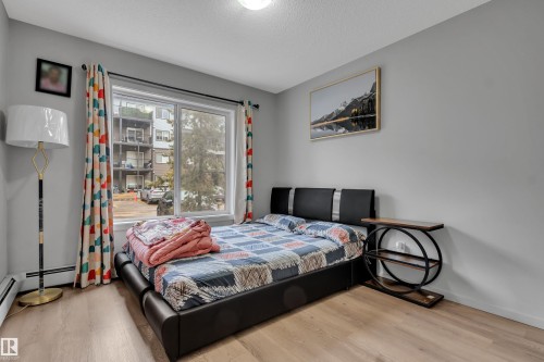 This inviting space features light wood-style flooring, a large window providing natural illumination, and a neutral wall color - 128 390 Windermere Road, Edmonton, AB - Indoor Photo Showing Bedroom