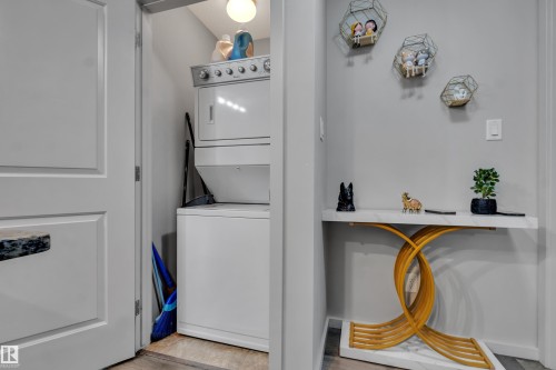 The property features a dedicated laundry area with a stacked washer and dryer, and a built-in wall niche with a console table - 128 390 Windermere Road, Edmonton, AB - Indoor Photo Showing Laundry Room
