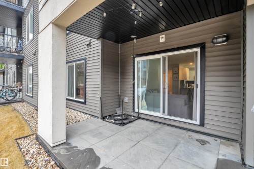 The property features an outdoor patio with concrete paving, adjacent to a landscaped area with grass and decorative stones - 128 390 Windermere Road, Edmonton, AB - Outdoor With Deck Patio Veranda With Exterior