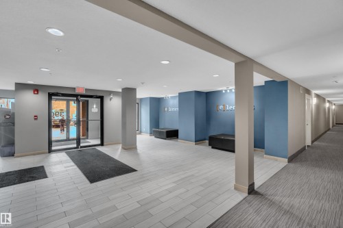 The property features a bright common area with light-colored flooring, recessed lighting, and a long hallway with carpeted flooring - 128 390 Windermere Road, Edmonton, AB - Indoor Photo Showing Other Room