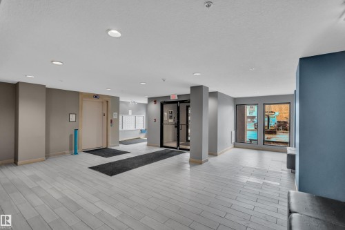 The property features a bright common area with light-colored tile flooring, recessed lighting, and large windows providing natural light - 128 390 Windermere Road, Edmonton, AB - Indoor Photo Showing Other Room