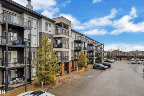 The property is a multi-story building featuring balconies and patios with dark railings, set against a blue sky with white clouds - 128 390 Windermere Road, Edmonton, AB - Outdoor