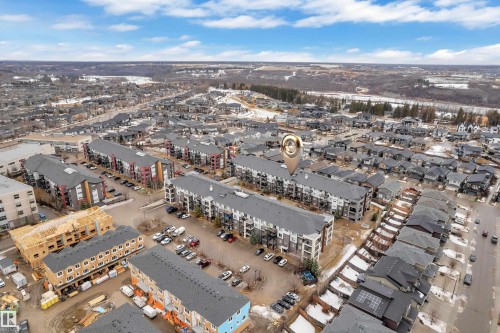 Aerial view showcasing a community with townhomes and apartment buildings, featuring paved roads and parking areas - 128 390 Windermere Road, Edmonton, AB - Outdoor With View