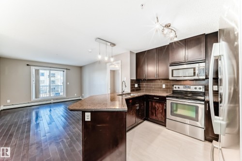The kitchen features dark wood cabinetry, stainless steel appliances, and a granite countertop island with a sink - 208 2204 44 Ave, Edmonton, AB - Indoor Photo Showing Kitchen With Double Sink